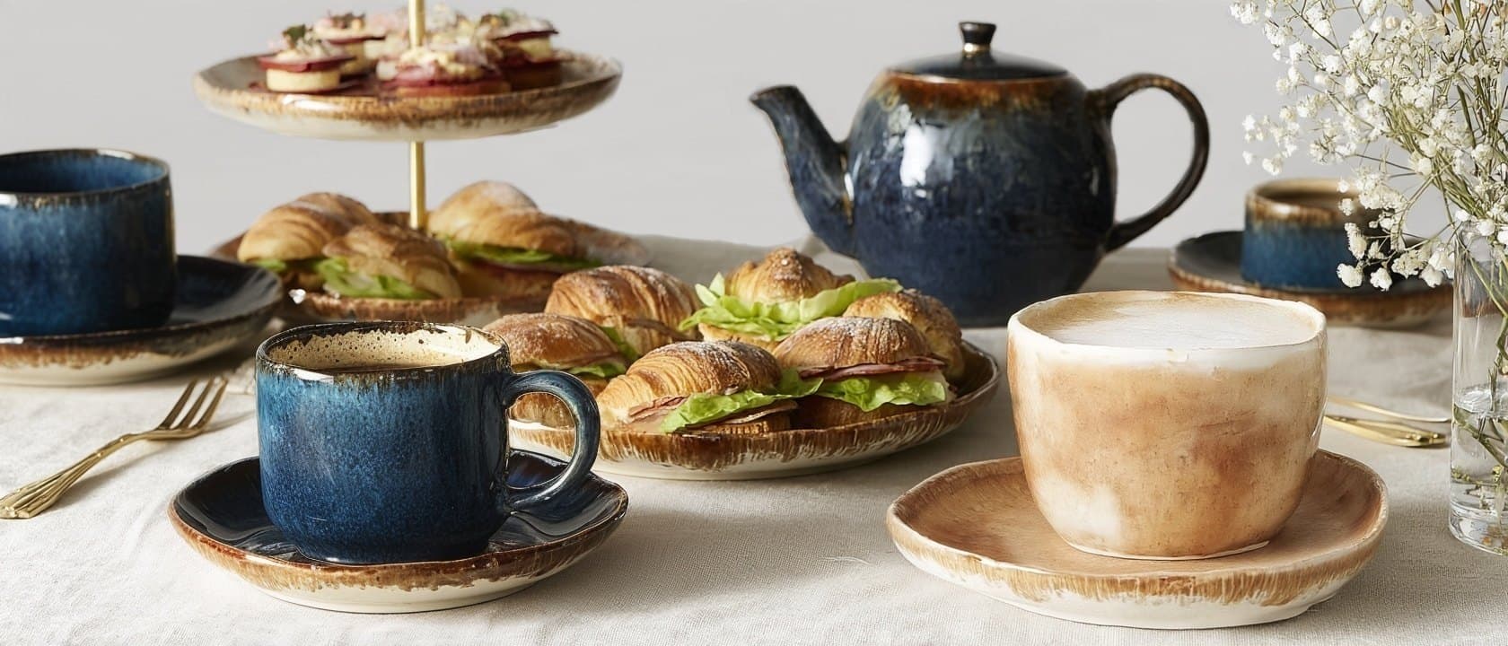 Stół z przerwą kawową: niebieska i karmelowa porcelana, dzbanek i mini croissanty z szynką